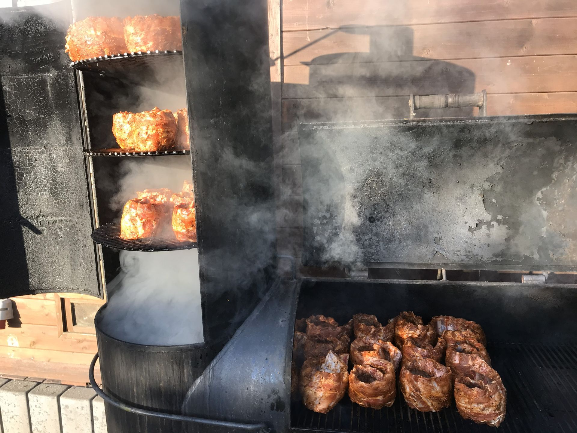 Barbecue-Smoker mit Rosten voller lecker aussehender Spare Rubs, aufsteigender Rauch. Außenaufnahme.