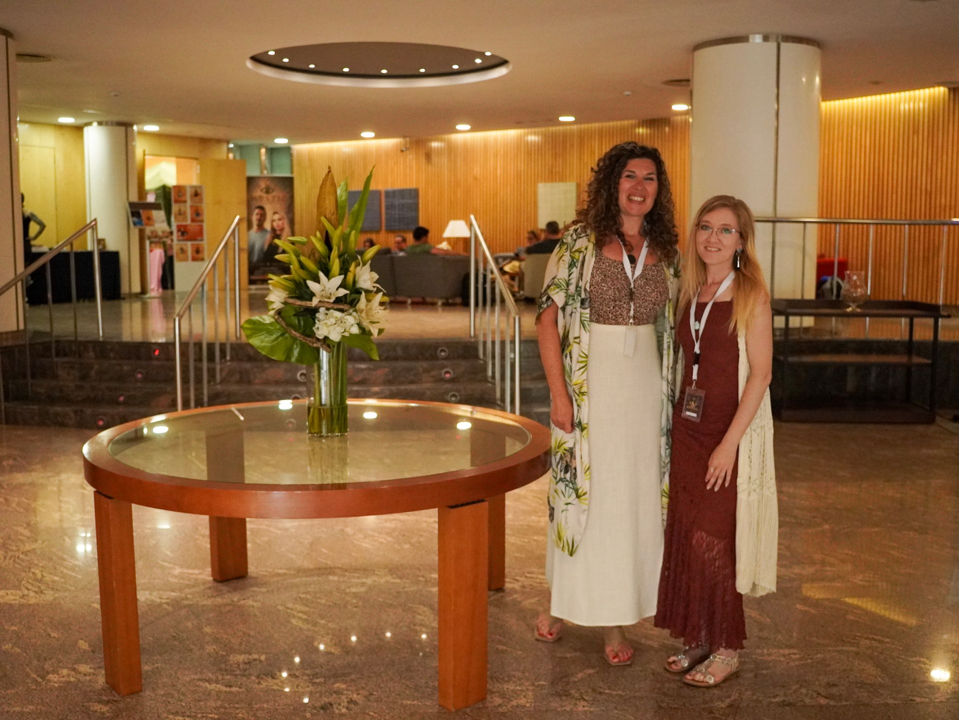Dos personas de pie en el vestíbulo de un hotel junto a una mesa redonda con flores.