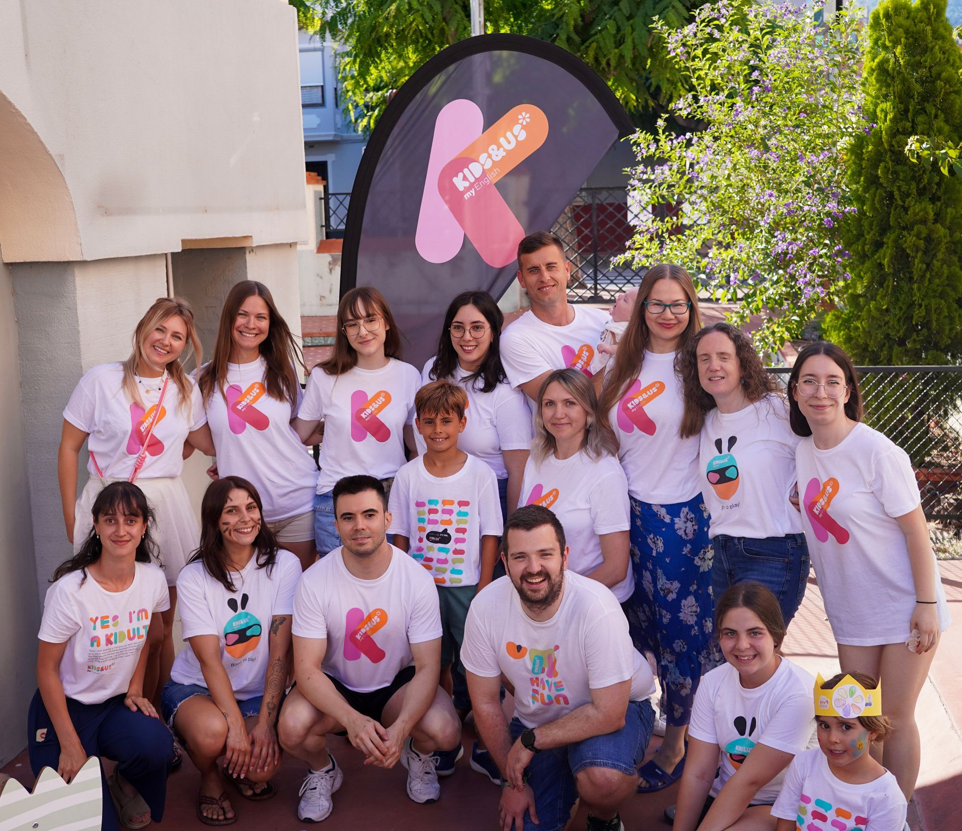 Grupo de personas con camisas blancas posando al aire libre junto a un cartel colorido y vegetación.