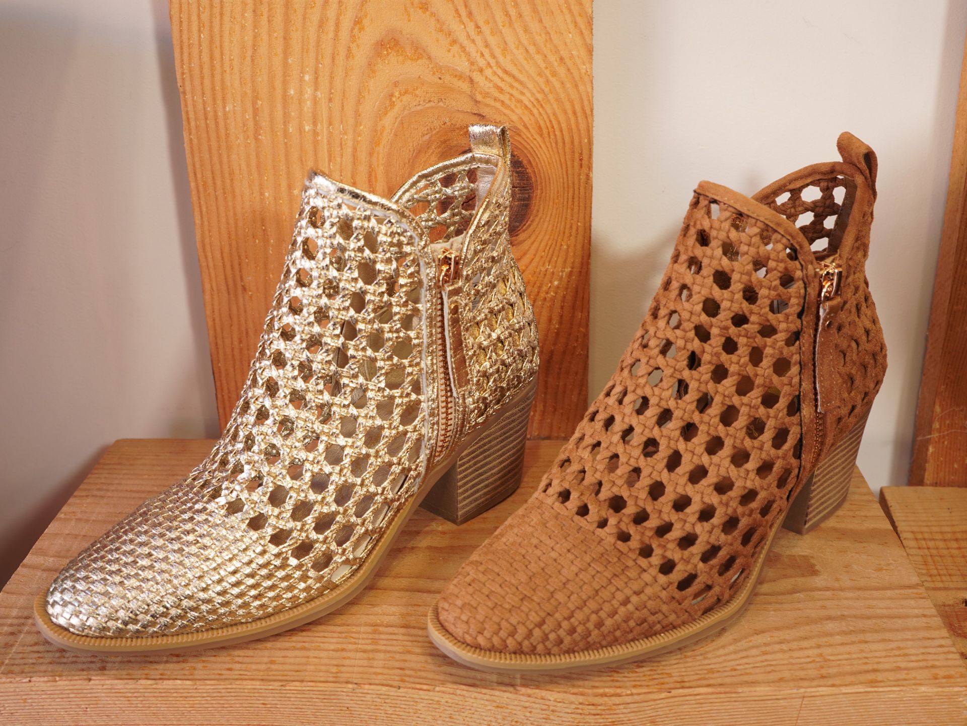 Dos botines de tacón perforado, uno dorado y otro color canela, sobre un suelo de madera.