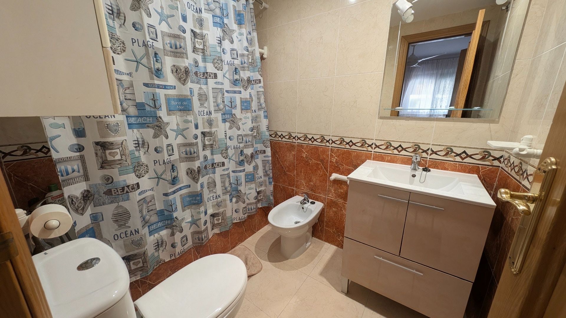 Baño pequeño con inodoro, mueble de lavabo, cortina de ducha estampada y ventana.