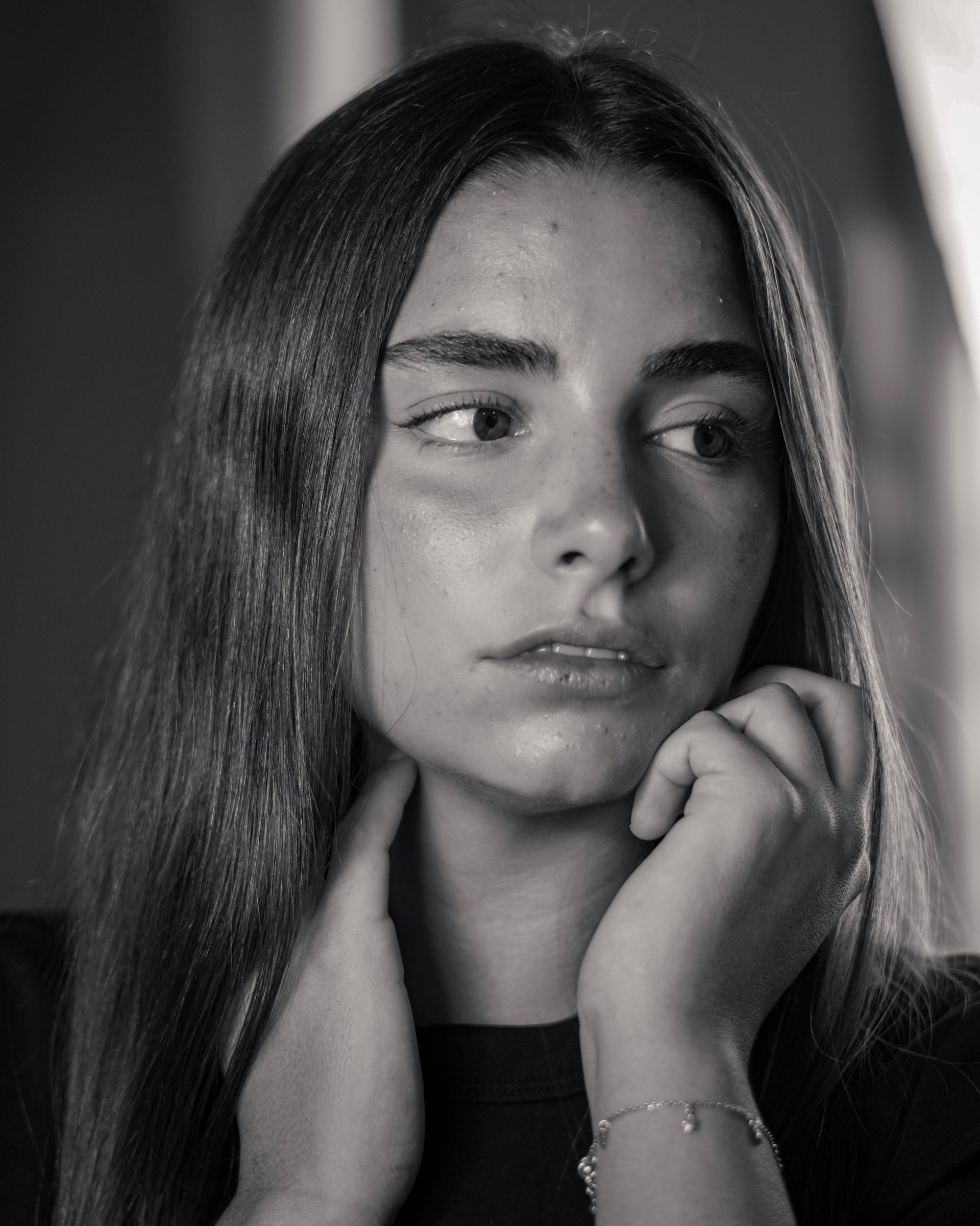 Retrato en blanco y negro de una persona, mirando hacia un lado con las manos cerca del rostro.