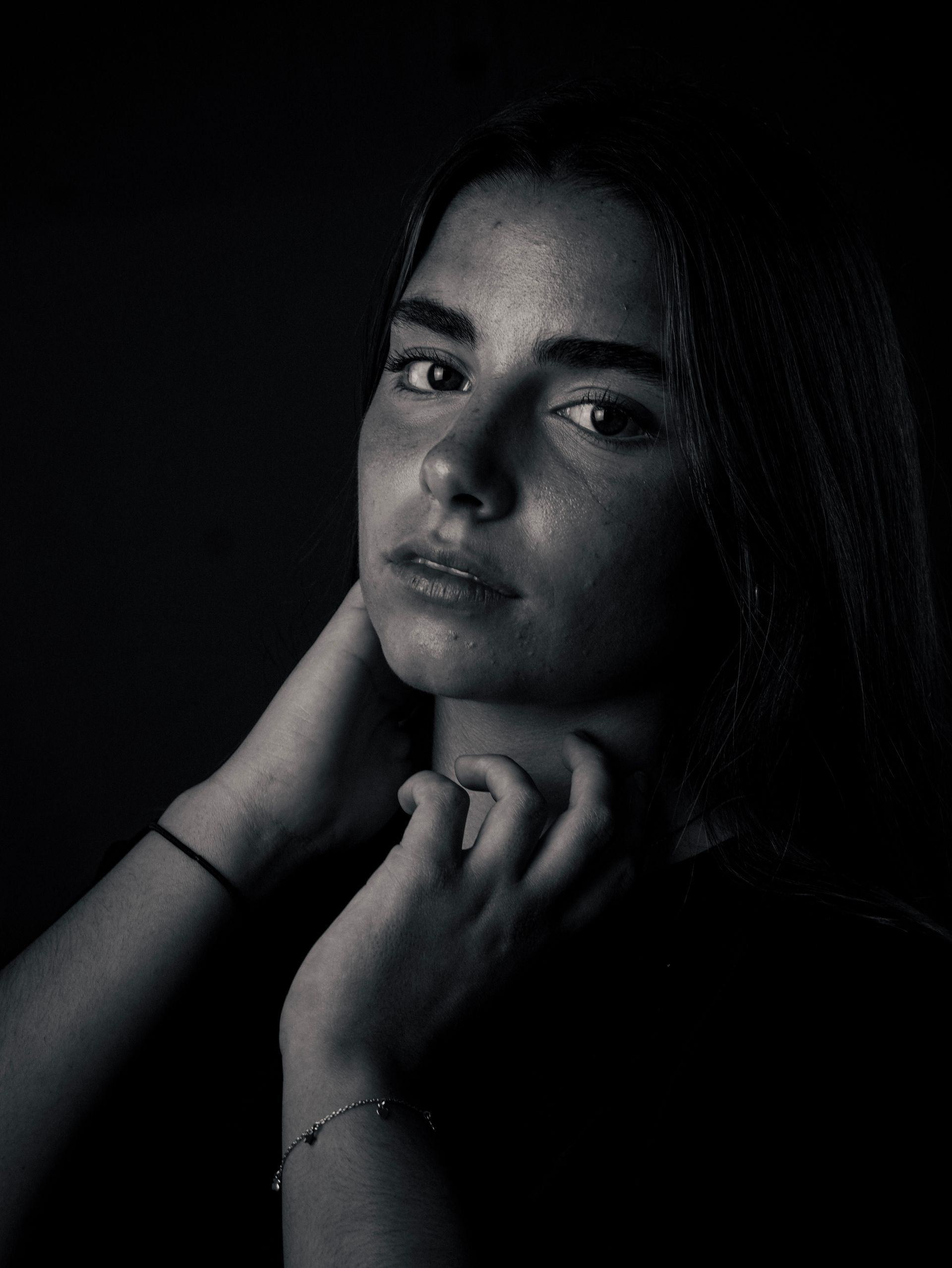 Retrato de una persona con poca luz, mirando a la cámara con las manos cerca del cuello.