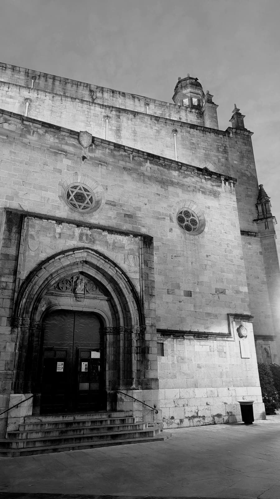 Vista en blanco y negro de la fachada de una iglesia de piedra con una gran puerta arqueada y escalones.