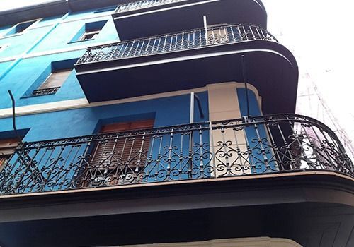 Edificio azul de varias plantas con balcones negros ornamentados y esquinas curvas, visto desde abajo.