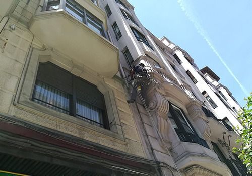 Vista desde un ángulo bajo de un alto edificio de apartamentos color beige contra un cielo azul.