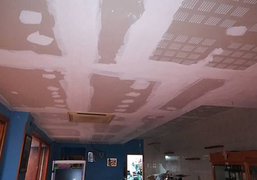 Techo de la habitación en obras con parches de pladur rosa, paredes azules y una abertura de ventilación.