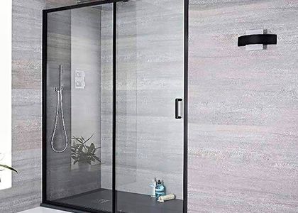 Mampara de ducha moderna de cristal en un baño con azulejos grises y aplique de pared negro.