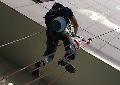 Persona descendiendo en rápel por un edificio con la ayuda de cuerdas, vista desde abajo contra un techo de baldosas.