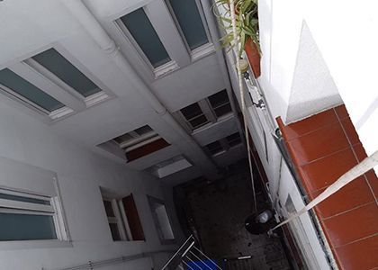 Vista de un patio estrecho entre edificios altos con paredes blancas, ventanas y un toldo a rayas en la parte superior.
