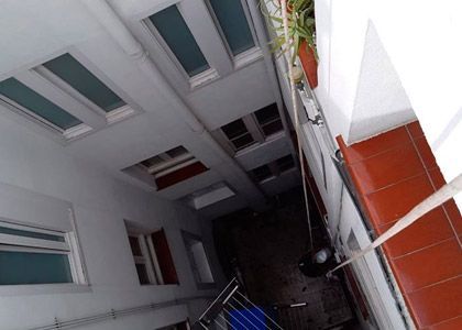 Vista desde el patio interior de un edificio estrecho con paredes blancas, ventanas verdes y detalles de azulejos naranjas.