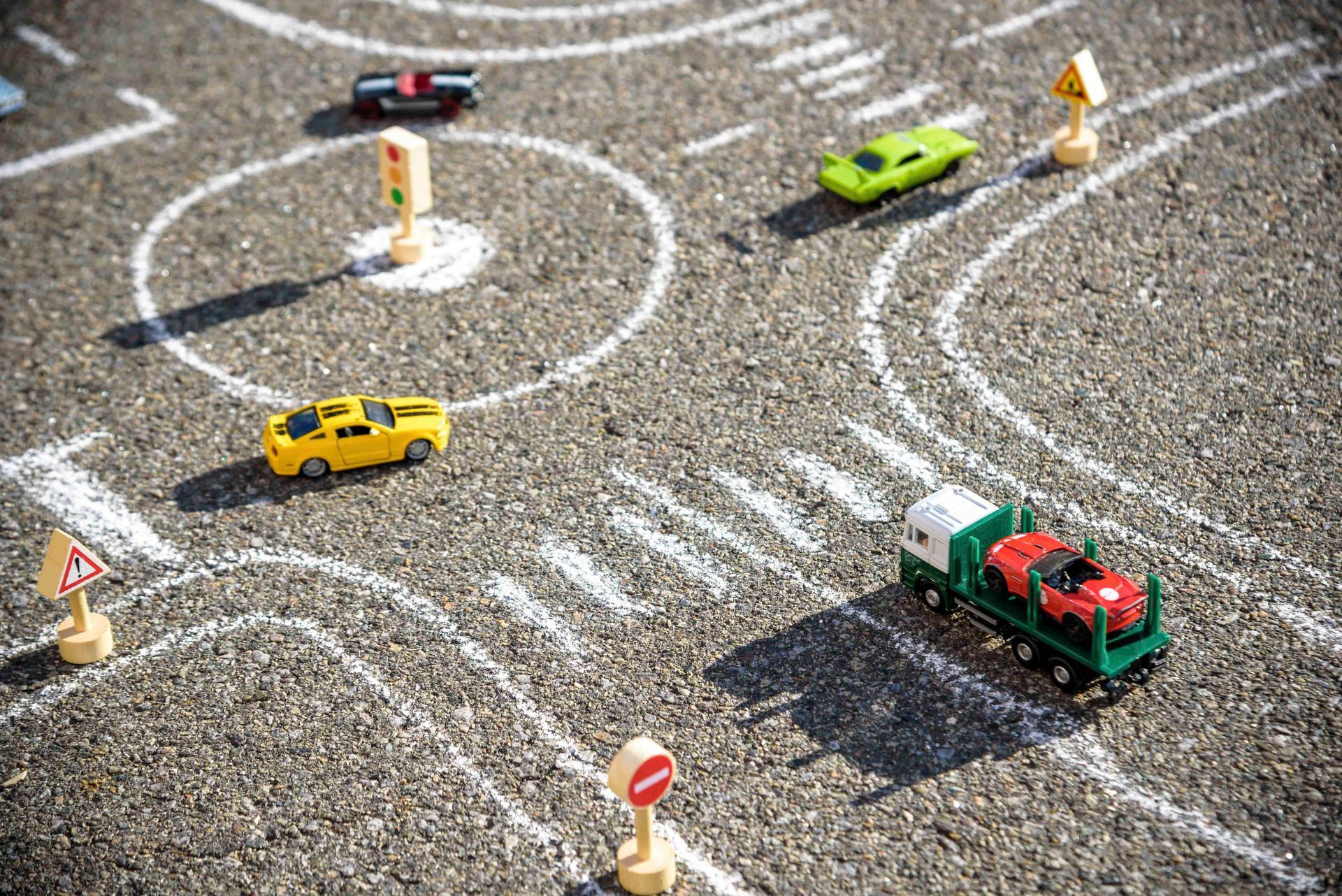 Spielzeugautos auf einer mit Kreide gezeichneten Rennstrecke mit Verkehrsschildern, darunter ein Taxi und ein grüner LKW