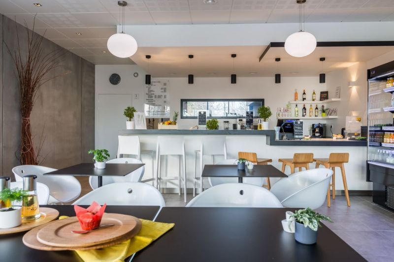 Salle de restaurant avec tables de différentes couleurs et cuisine ouverte avec chaises hautes