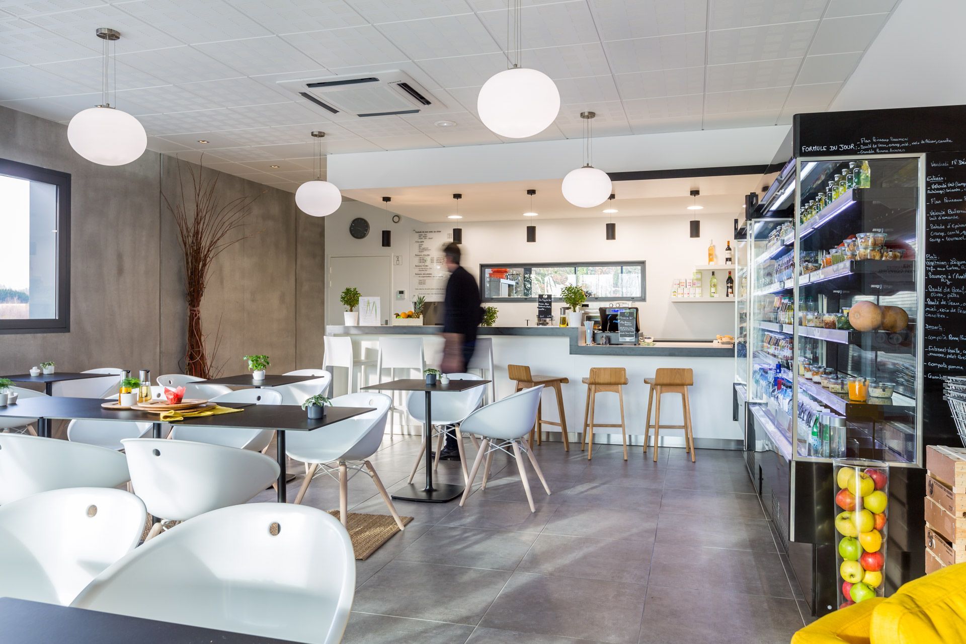Salle de restaurant avec tables de différentes couleurs et cuisine ouverte