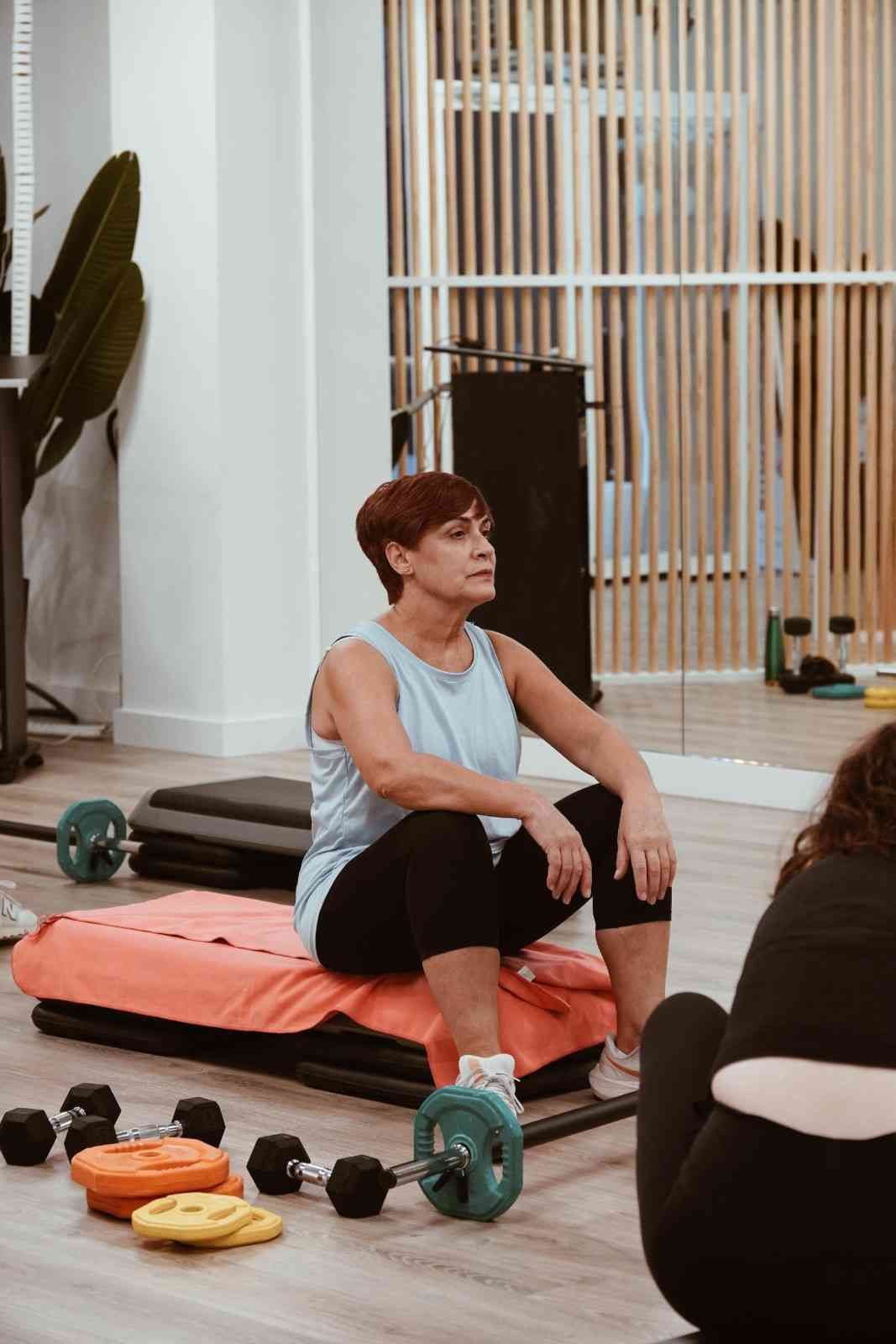 Mujer descansando sobre una colchoneta de gimnasia junto a unas mancuernas en un gimnasio.