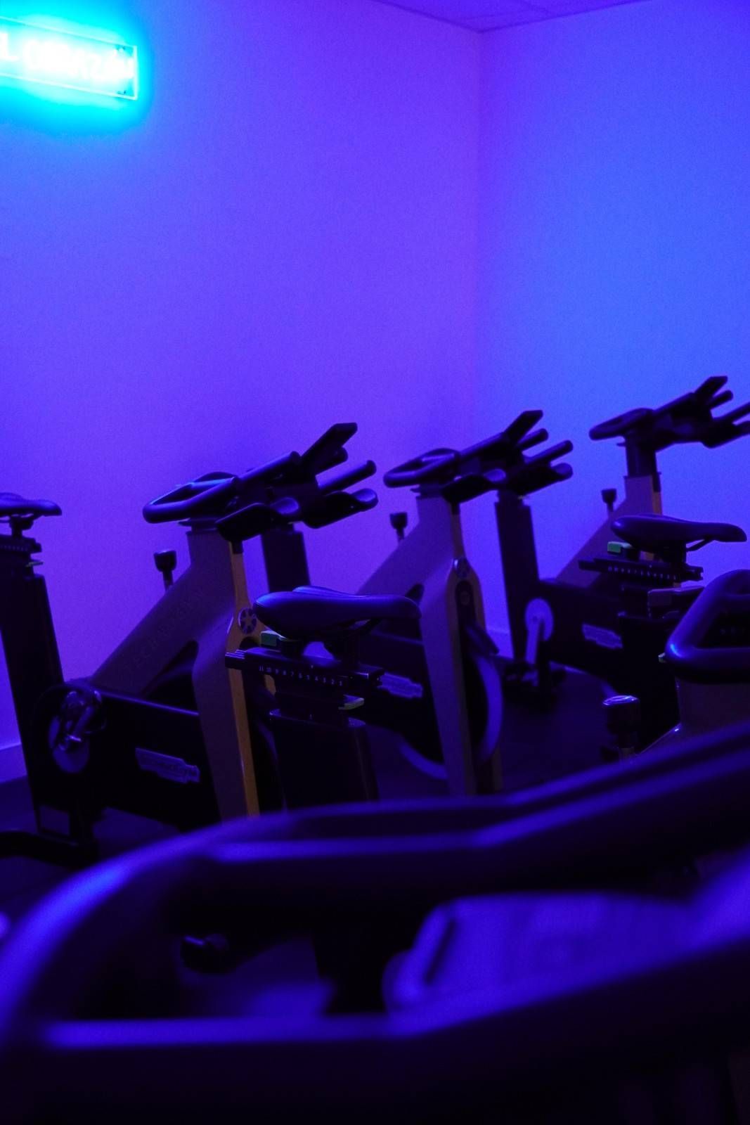 Gimnasio iluminado con luz violeta y varias bicicletas estáticas alineadas en una sala.