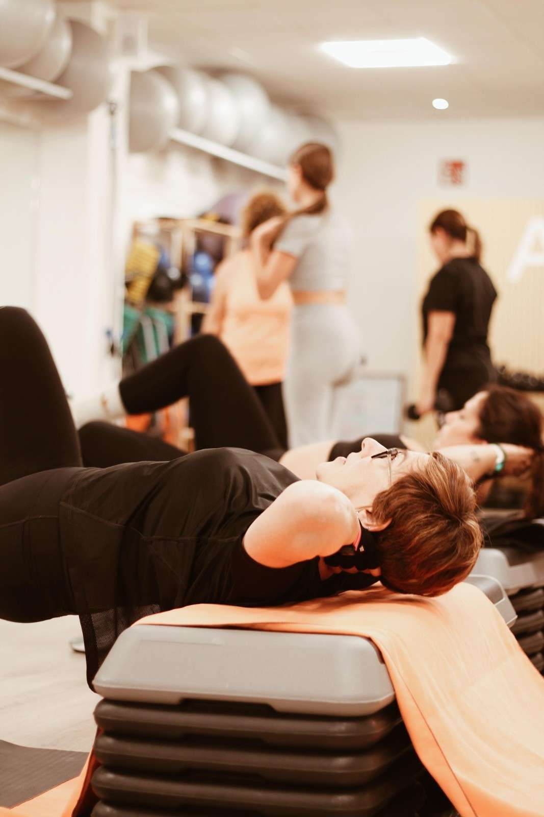 Varias personas se ejercitan en un gimnasio, una de ellas haciendo planchas laterales en un banco.