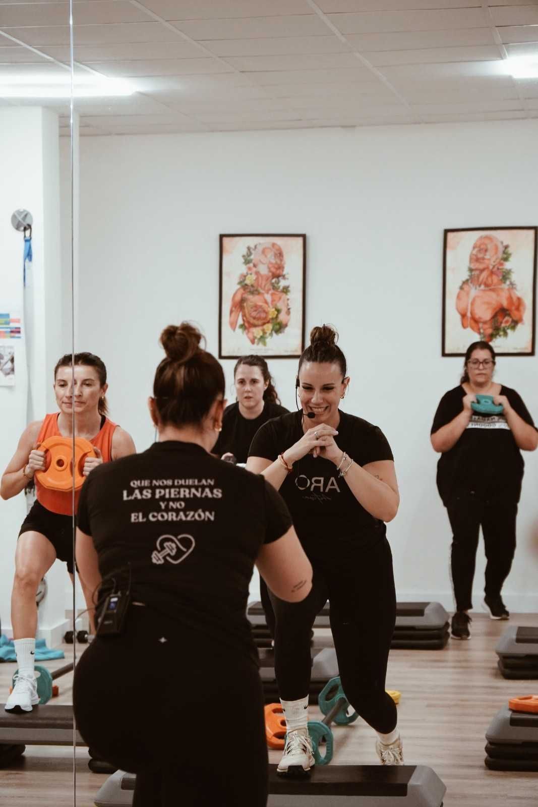 Mujeres con ropa deportiva participando en una clase de fitness grupal con plataformas de step en un estudio luminoso.