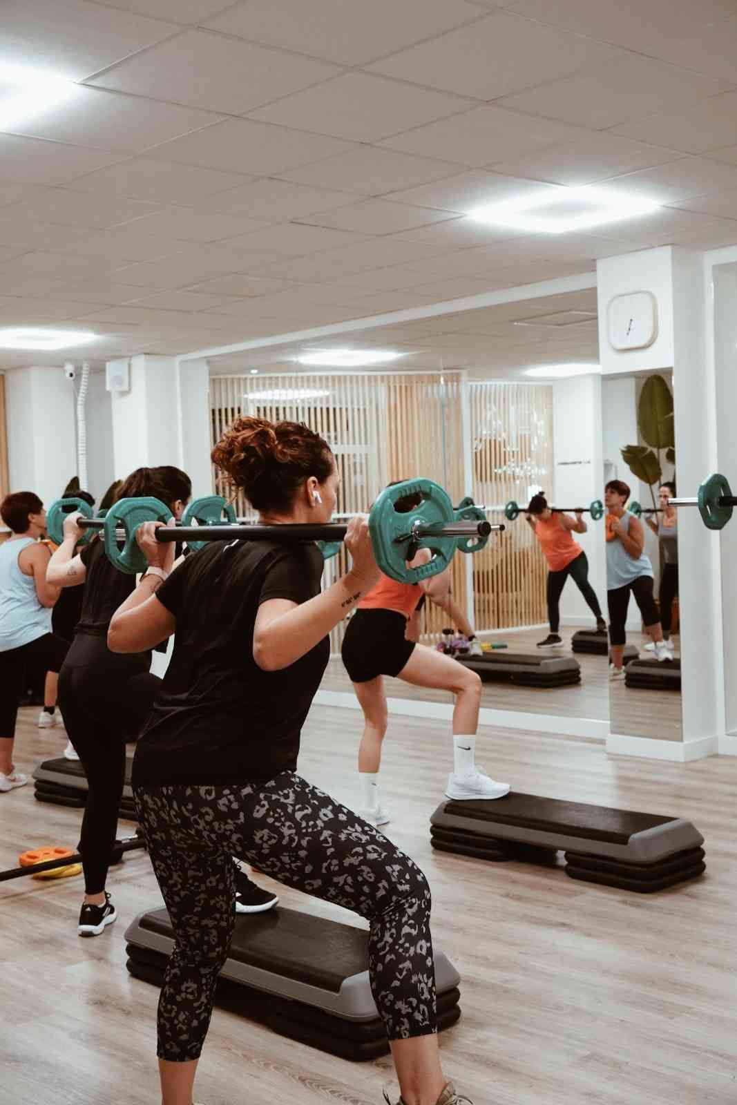 Personas haciendo ejercicios aeróbicos con pesas en un gimnasio con espejos.