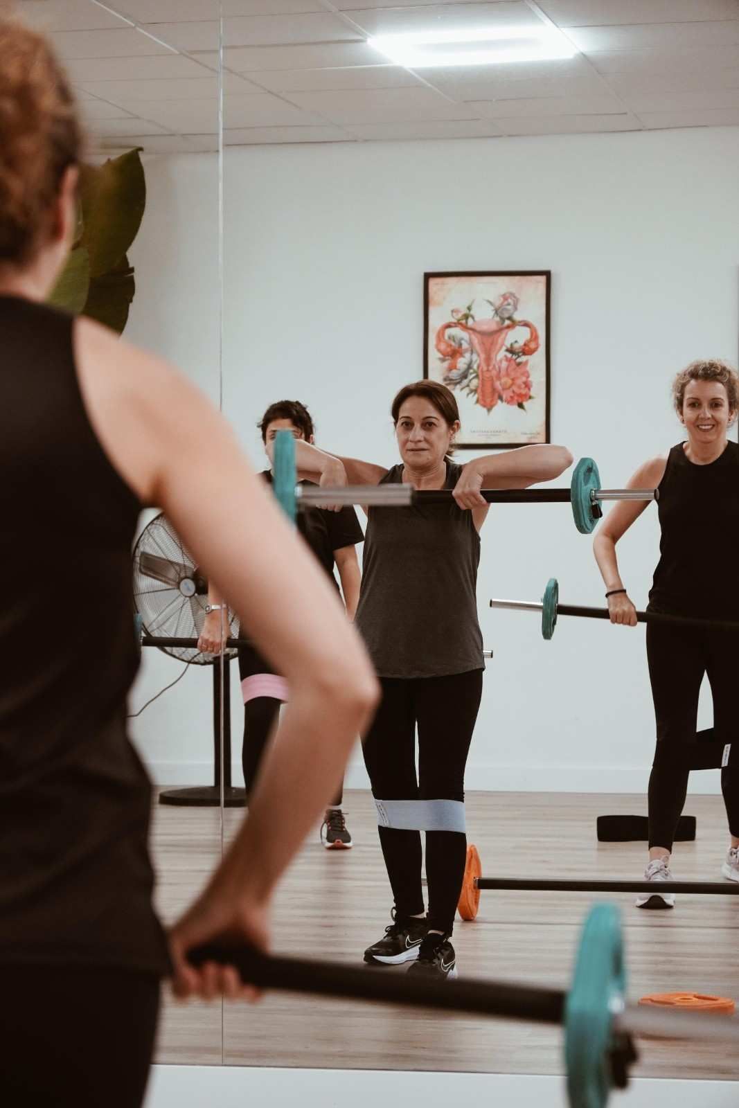 Varias personas realizan un entrenamiento con barra en un estudio con espejos, con una persona .