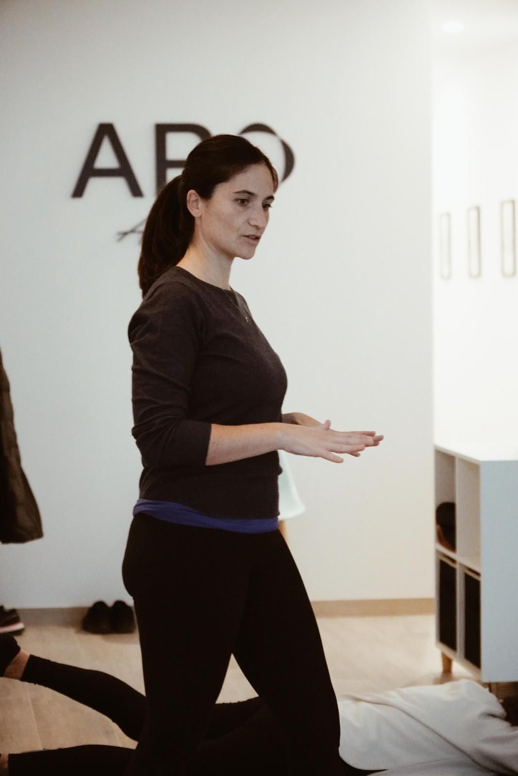 Mujer de pie en el interior de un estudio, sosteniendo papeles y mirando hacia la izquierda, con un gran logotipo.