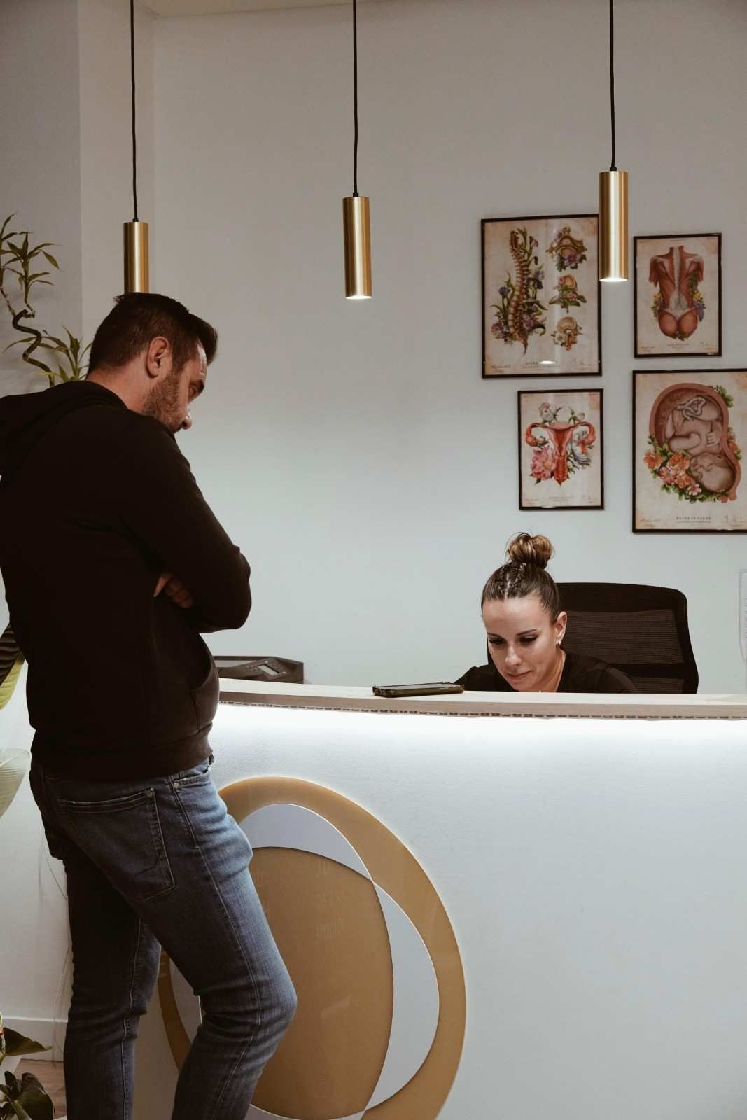 Un hombre permanece de pie junto a un mostrador de recepción blanco mientras una recepcionista trabaja detrás de él.