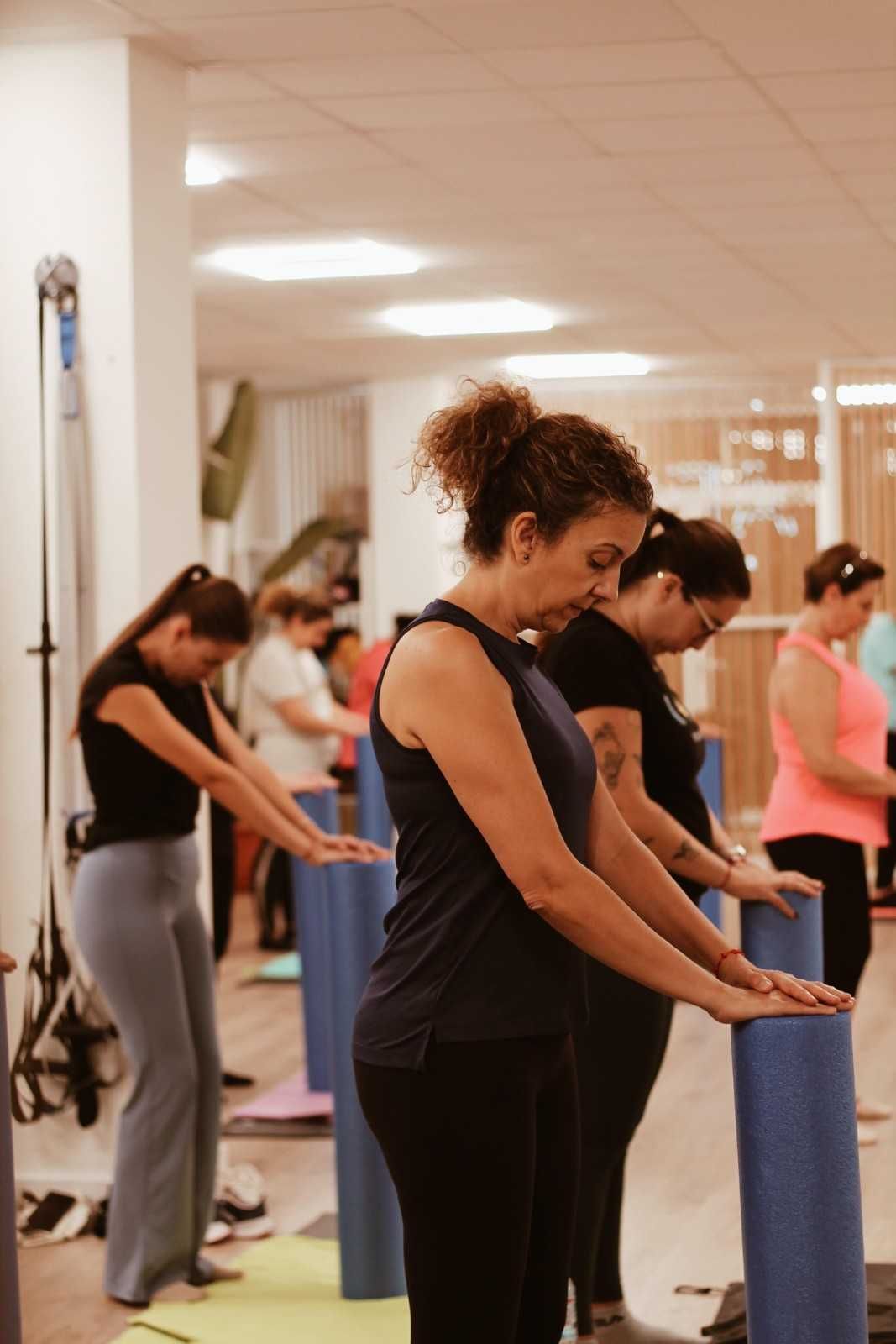 Personas haciendo ejercicio en un estudio, de pie junto a barras acolchadas azules e inclinándose hacia adelante.