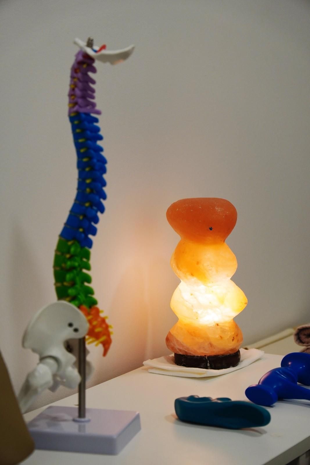 Expositor de mesa con un modelo de columna vertebral colorido, una lámpara naranja brillante y objetos azules.