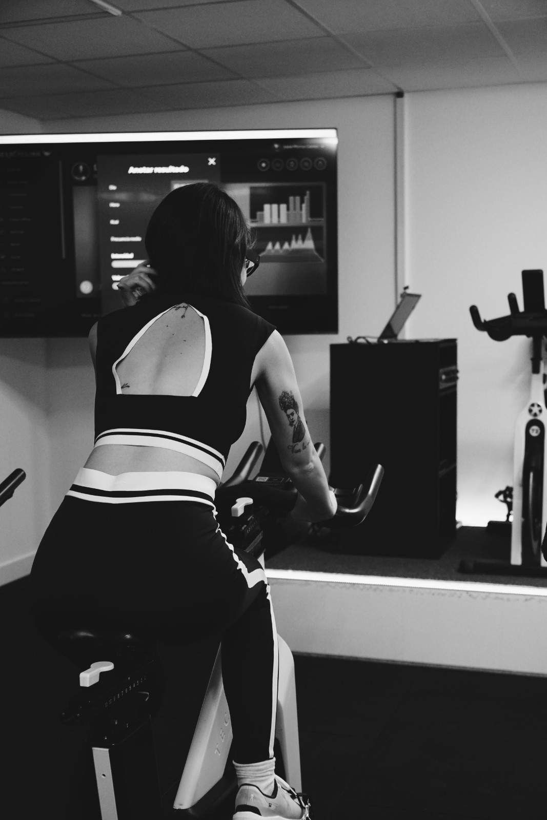 Una persona se está ejercitando en un gimnasio, inclinándose hacia una pantalla que muestra datos de su entrenamiento.