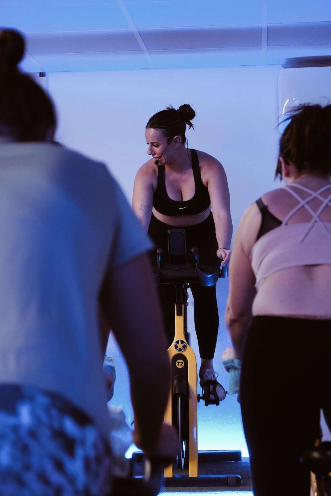 Personas haciendo ejercicio en bicicletas estáticas en un estudio interior iluminado con luz azul.