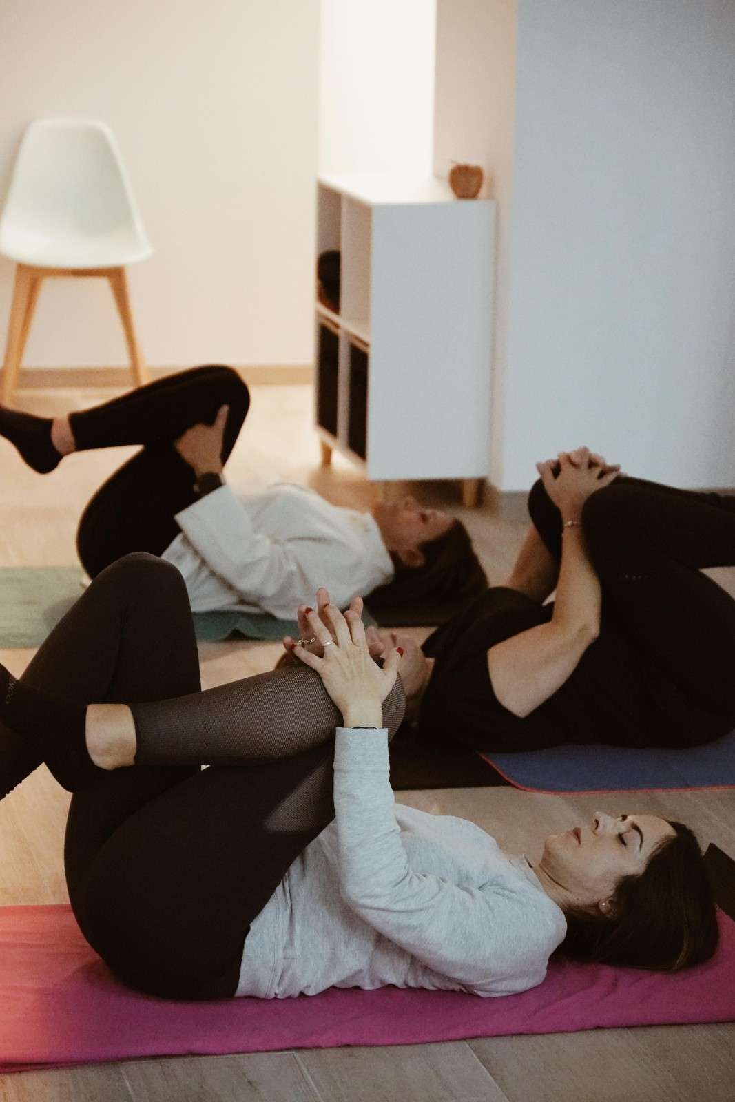 Personas haciendo estiramientos de yoga en el suelo sobre colchonetas en un estudio luminoso.