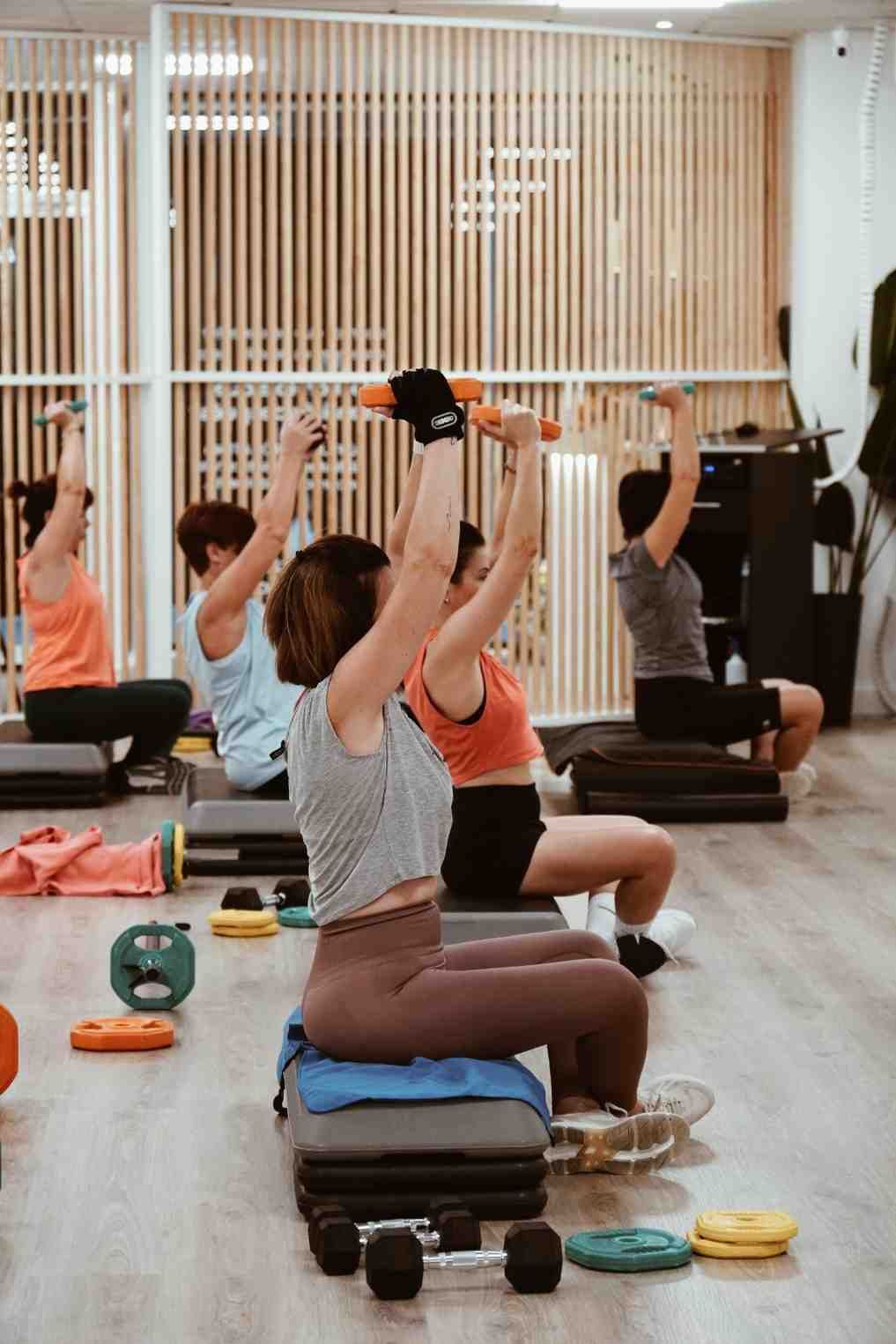 Personas realizando una clase de yoga sentadas en un estudio luminoso, con los brazos levantados sobre esterillas y bloques.
