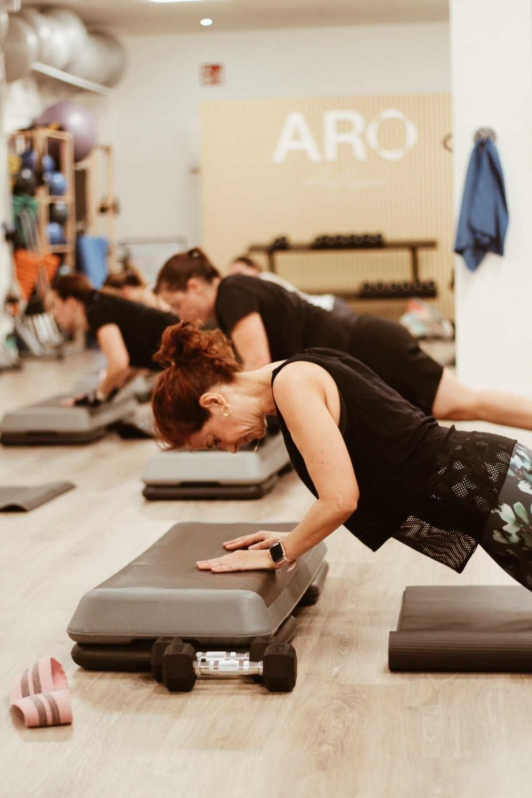 Personas haciendo ejercicios de plancha lateral sobre colchonetas en un luminoso gimnasio.