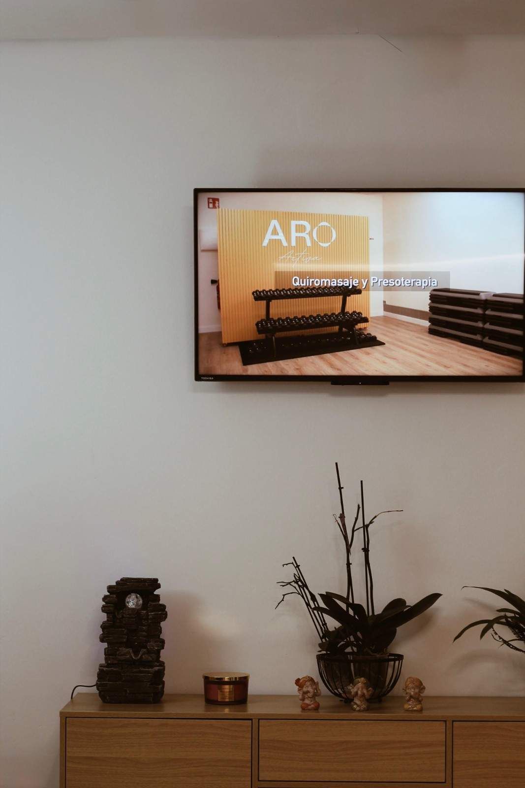 Vestíbulo moderno con televisor de pared que muestra una escena de auditorio sobre un aparador de madera decorativo.