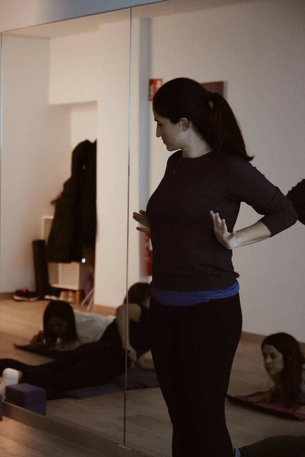 Una mujer está de pie en un estudio con espejos, con las manos en las caderas, mientras otras personas.