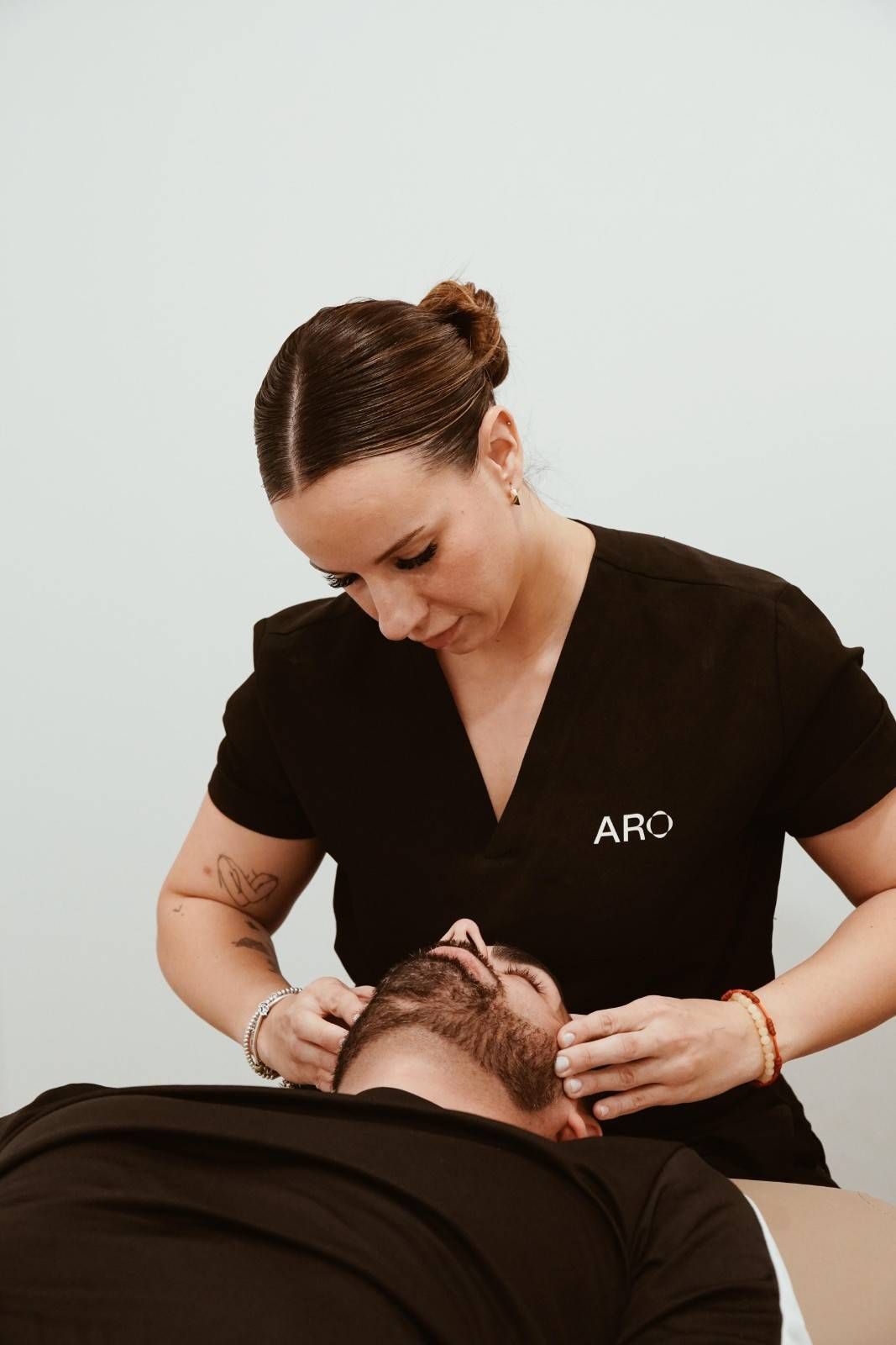 Mujer con bata oscura realizando un tratamiento facial a una clienta en una camilla de tratamiento.