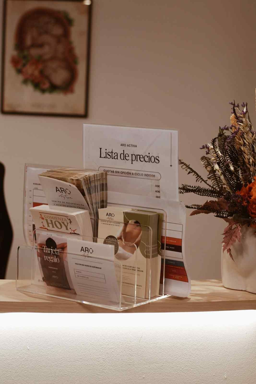 Un expositor de folletos sobre un mostrador, junto con panfletos sobre el cuidado de la piel y un arreglo floral.