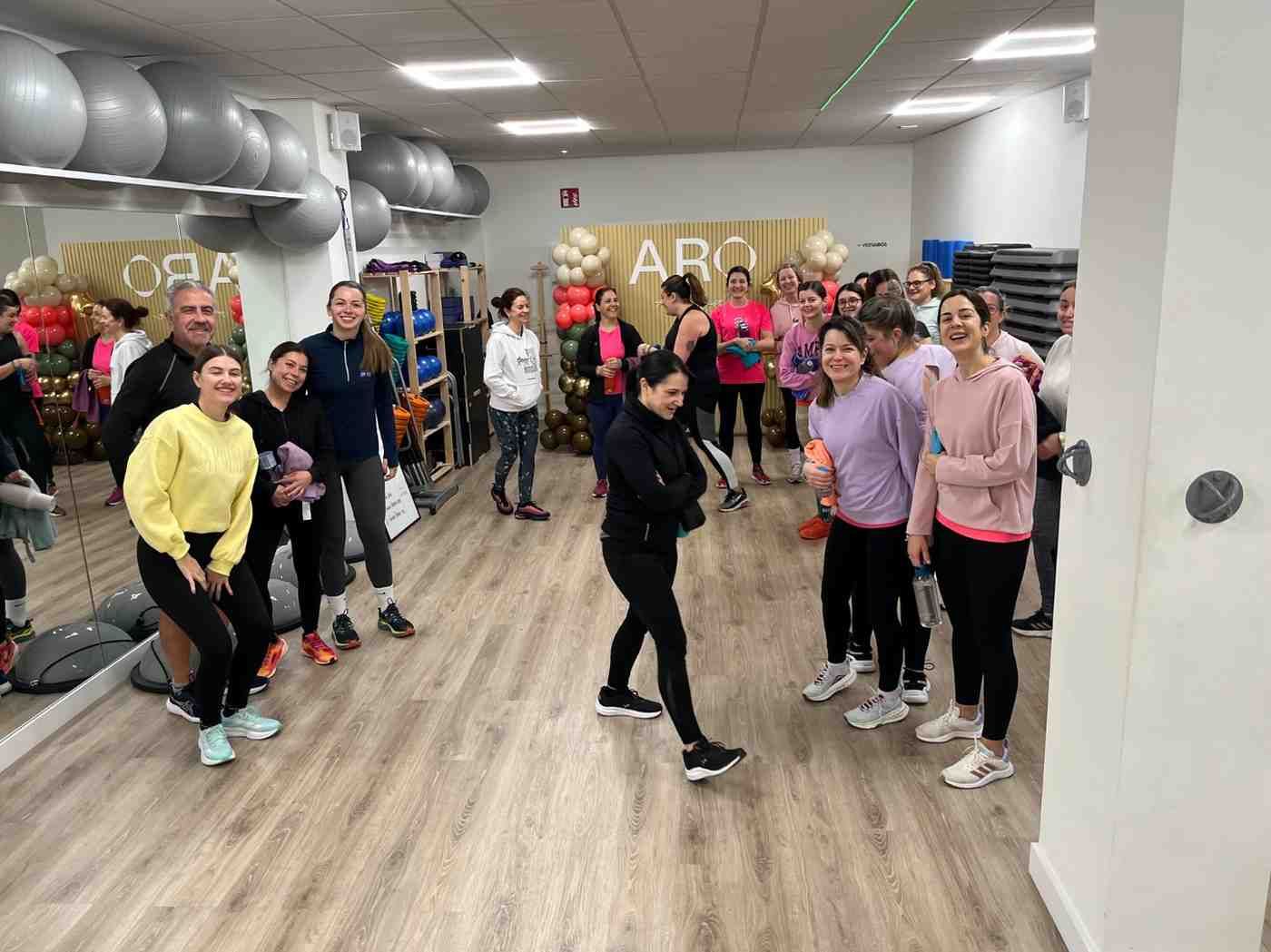 Clase de ejercicio en grupo en un estudio con espejos, donde las personas forman un semicírculo alrededor de un instructor.