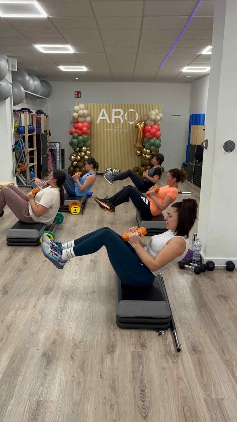 Personas haciendo ejercicio sobre colchonetas en un luminoso gimnasio interior con espejos y decoración.