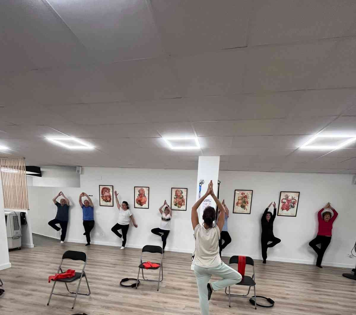 Una persona se estira en un banco de un gimnasio mientras otras personas hacen ejercicio al fondo.