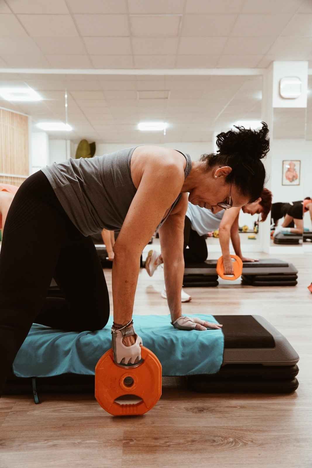 Mujer realizando ejercicios con pesas en un banco en un gimnasio.
