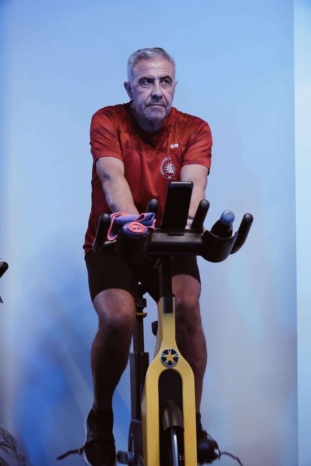 Hombre montando en una bicicleta estática, con una camiseta roja, sobre un fondo azul.