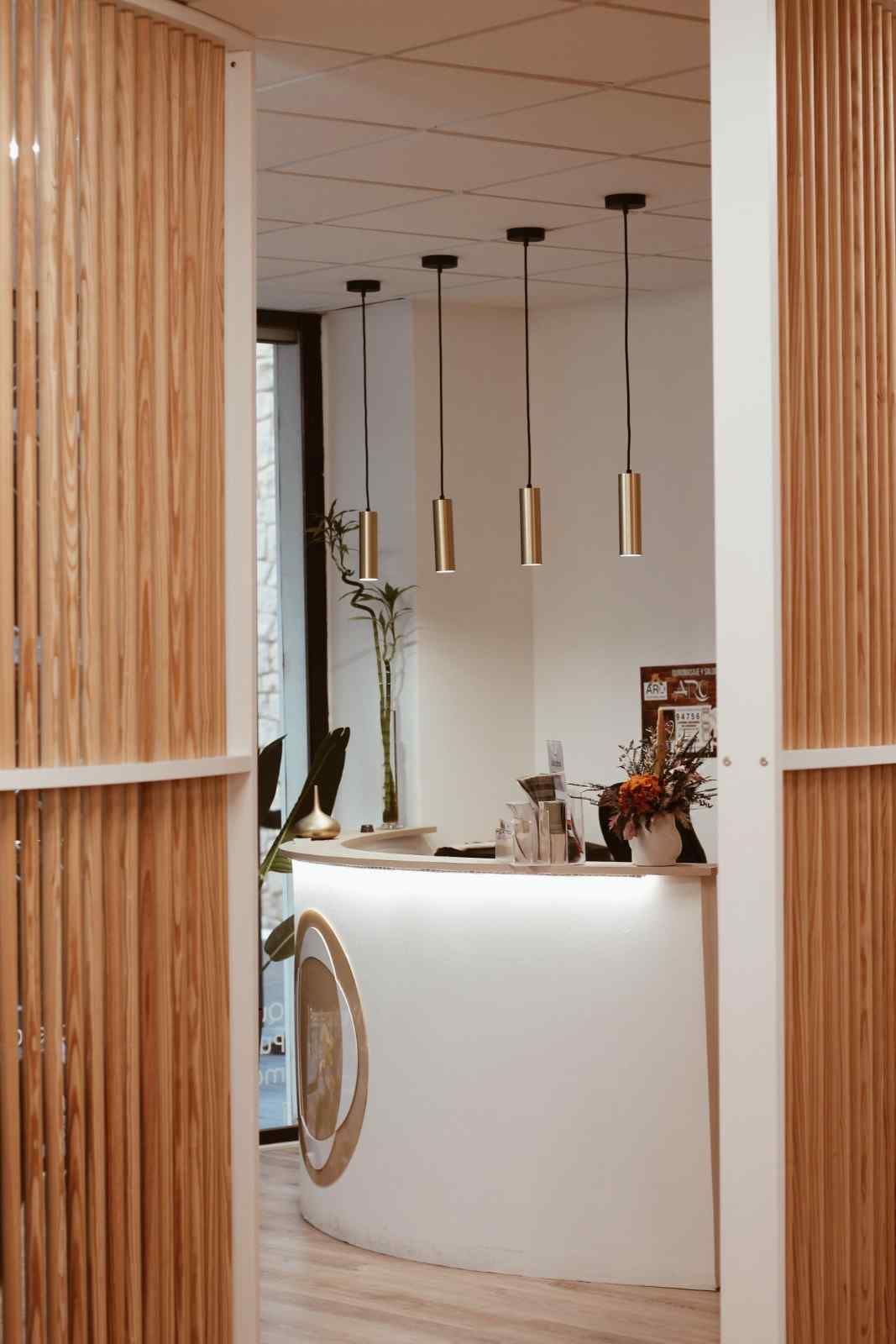 Elegante rincón de bar con lámparas colgantes, paredes revestidas de listones de madera y una barra blanca curva.