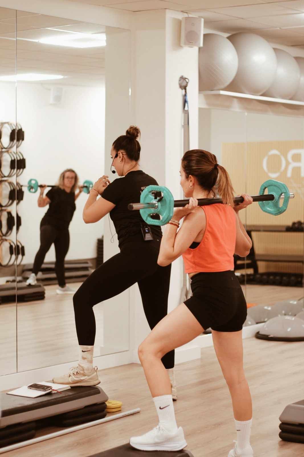 Dos personas haciendo ejercicio con barras en un gimnasio con espejos.