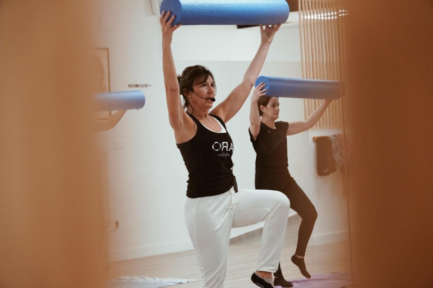 Personas haciendo ejercicio con rodillos de espuma azules en un estudio luminoso.