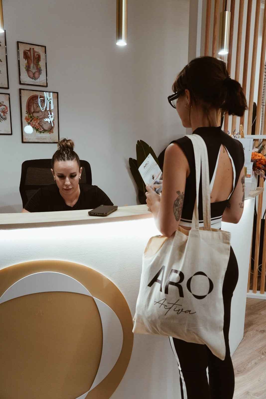Mujer vestida de negro de pie junto al mostrador de una peluquería, frente a una recepcionista.