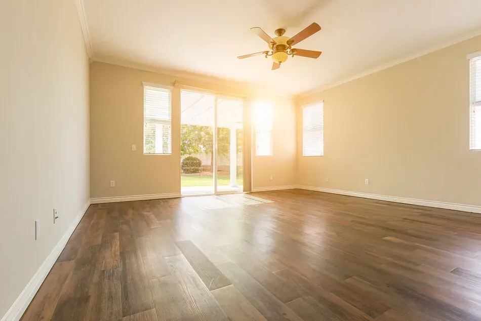 Una sala de estar vacía con pisos de madera y un ventilador de techo.