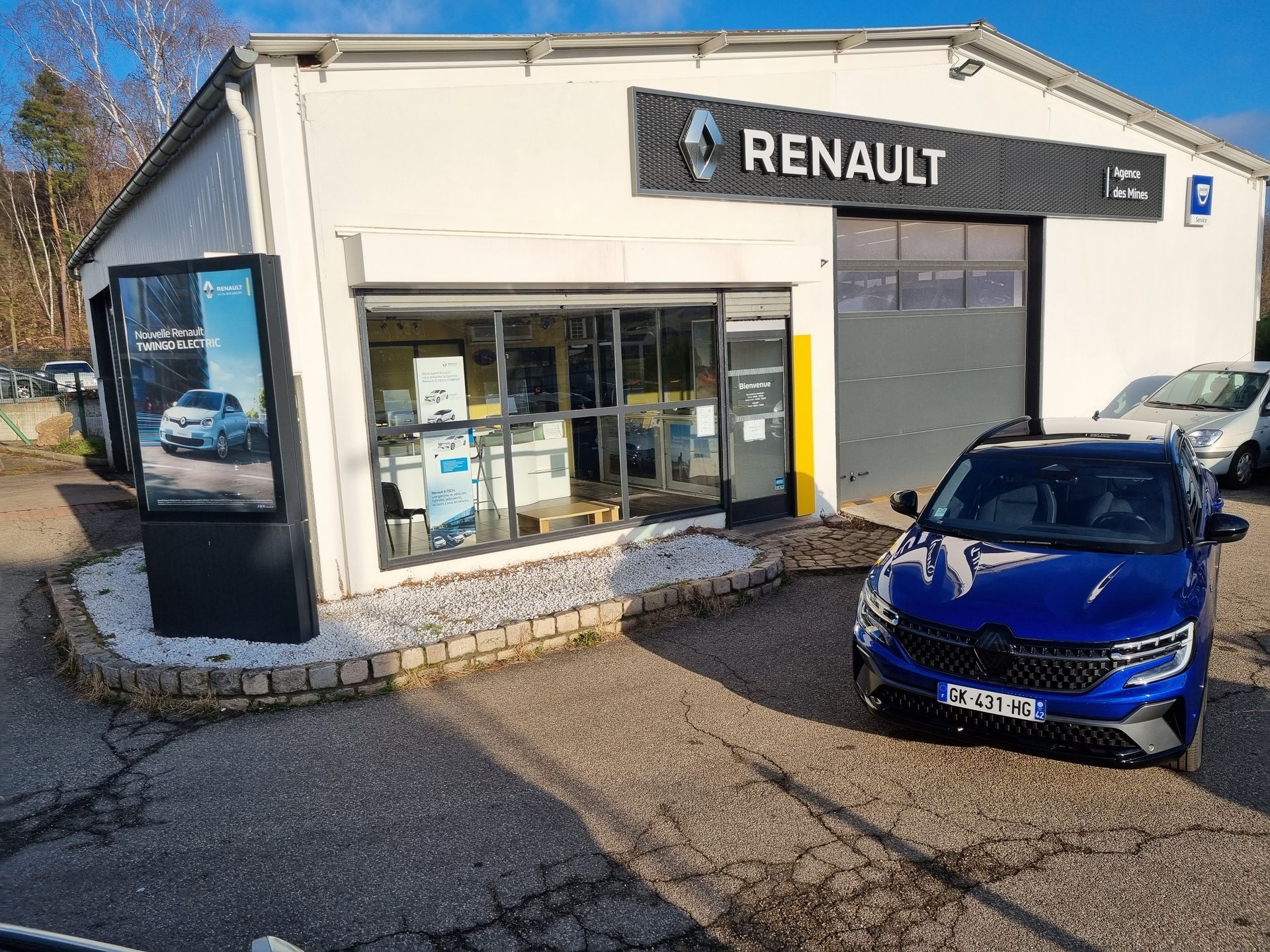 Un véhicule bleu devant un garage Renault.