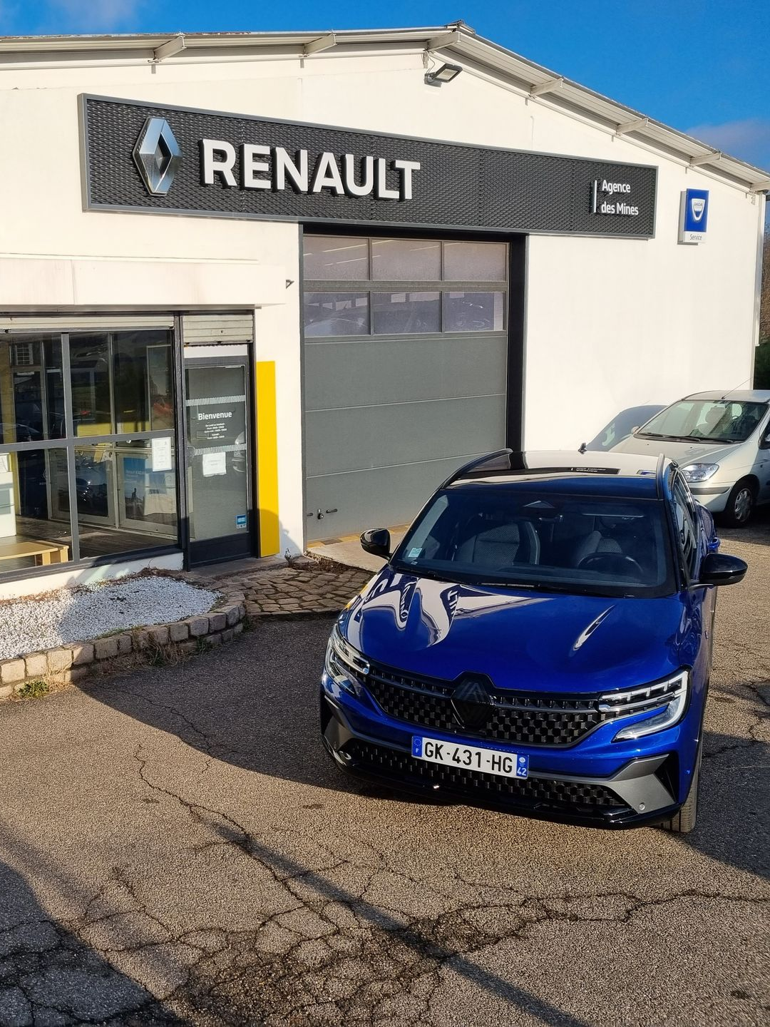 Voiture neuve bleue devant le garage.