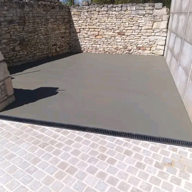 Patio entouré de murs en pierre, avec un sol gris lisse et un pavage en briques claires au premier plan.